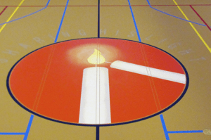 The Messiah logo (two lit candles in an orange circle) on the floor of the gym
