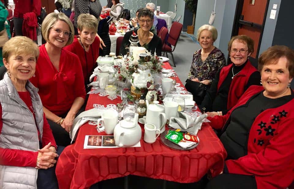Group of women mostly dressed in red sitting at a table for holiday tea.